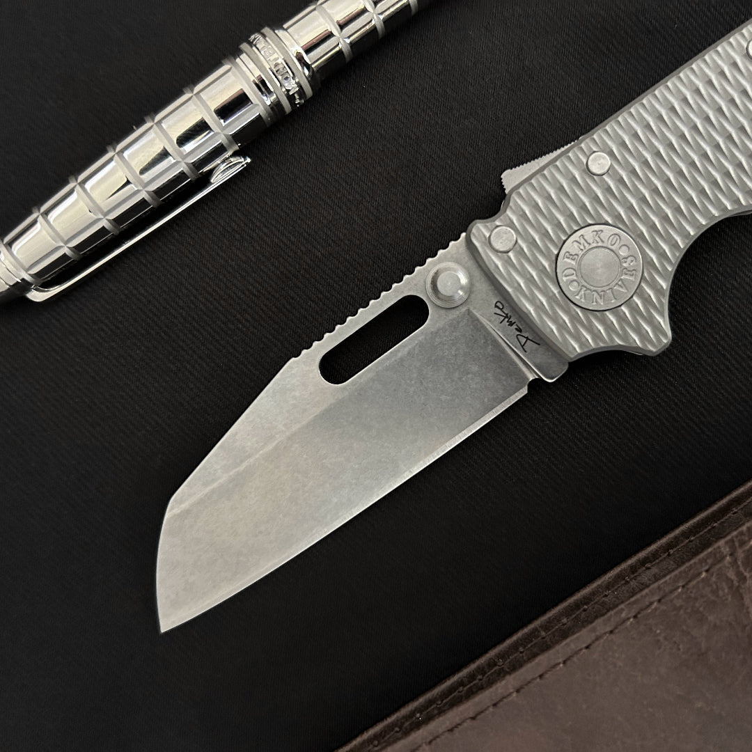 AD20.5 CPM 20CV shark foot folding knife pictured with a mont blanc pen and brown leather wallet.