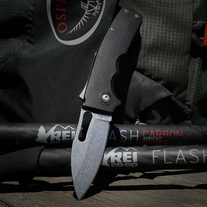 Shark-Cub slicer shark folding knife on a REI Flash Carbon Series hiking sticks with an osprey backpack in the background.
