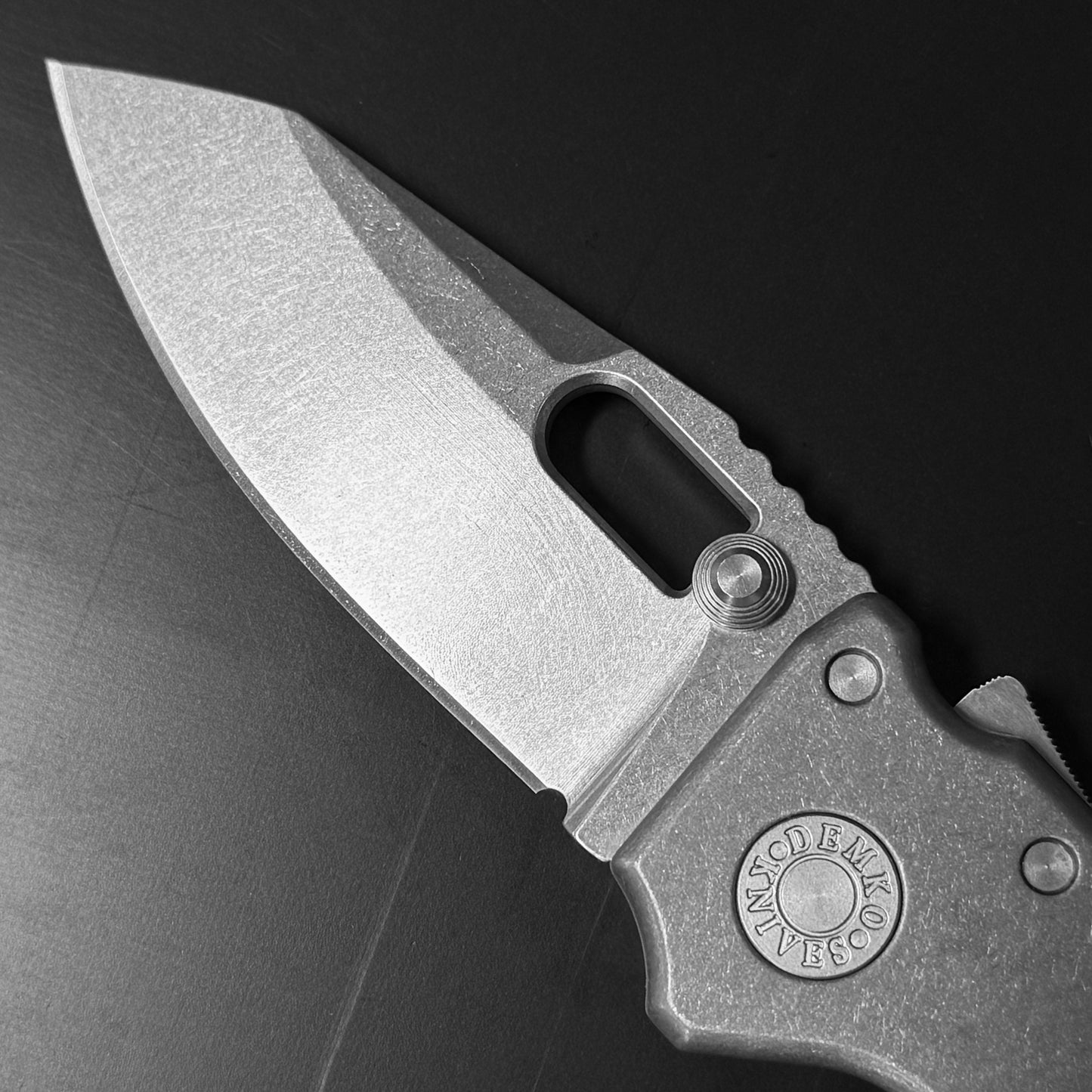 Demko AD20 Compact Knife with MagnaCut steel blade, smooth titanium handle, and Demko Shark-Lock, closeup of blade on dark background.