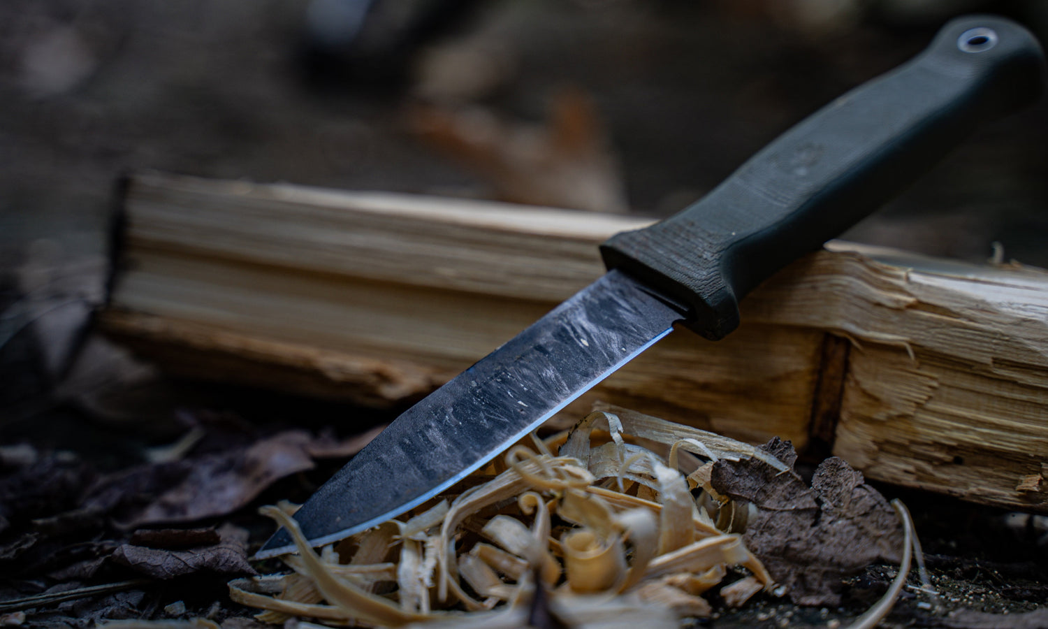 Armiger 4 fixed blade being used to prepare campfire materials in an outdoor scenario.