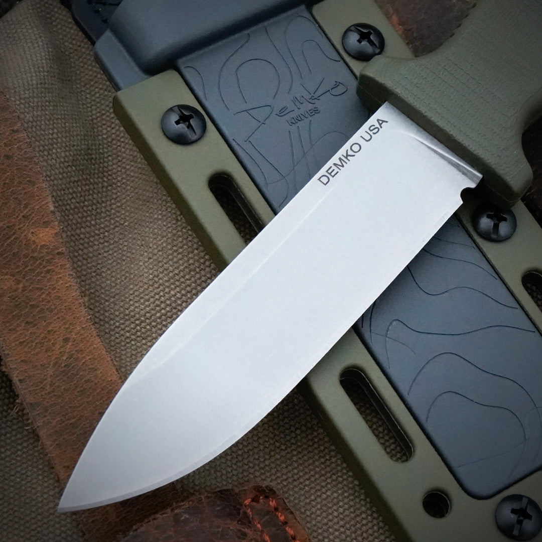 Armiger 4 fixed blade hunting knife with an OD Green handle and sheath laying on a canvas backpack.