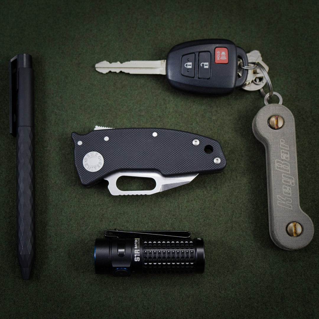 Everyday carry carry setup featuring the nano-shark, flashlight, pen, and keybar on a green background.