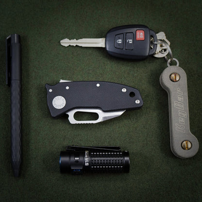 Everyday carry carry setup featuring the nano-shark, flashlight, pen, and keybar on a green background.