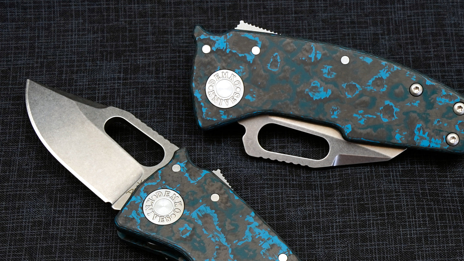 Two Nano-Shark Arctic Storm folding knives with blue and black fat carbon handles on a dark textured background.