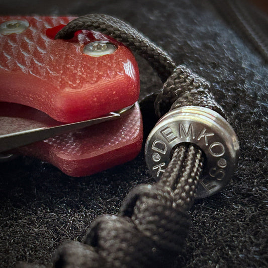 Close-up of a Demko titanium bead on a paracord lanyard attached to an AD20 folding knife.