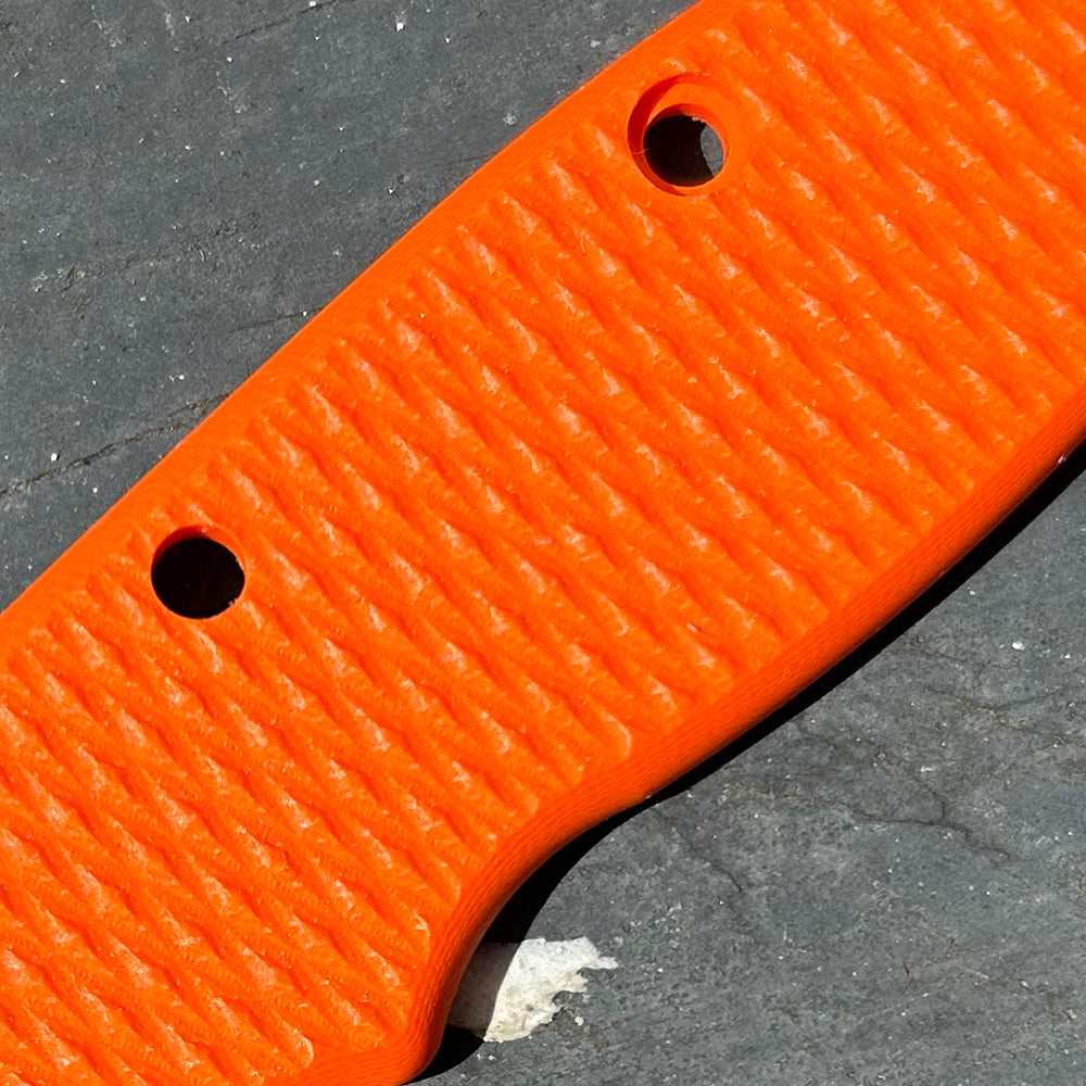 Close-up of an orange milled G10 scale with a diamond pattern texture.